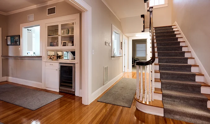 An interior view of a medical office hallway and reception area. It shows polished hardwood floors, a white-cabinetry reception desk with a built-in glass-door cooler, and a carpeted staircase with a dark wooden banister leading to a second floor. - in Tampa, FL